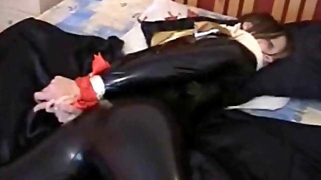 Latex-clad brunette with an awesome body tied up on her bed