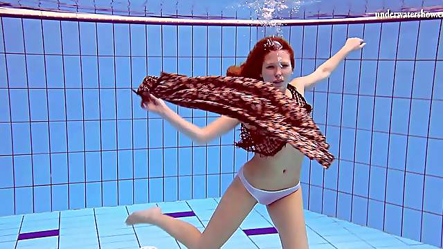 Slim redhead looker dives around the pool in the nude
